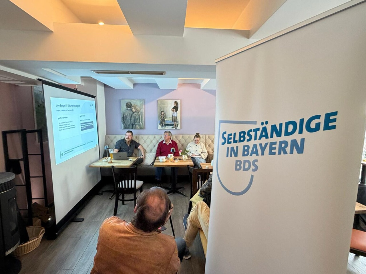 Bastian giving an AI talk with participants and a banner reading Selbständige in Bayern